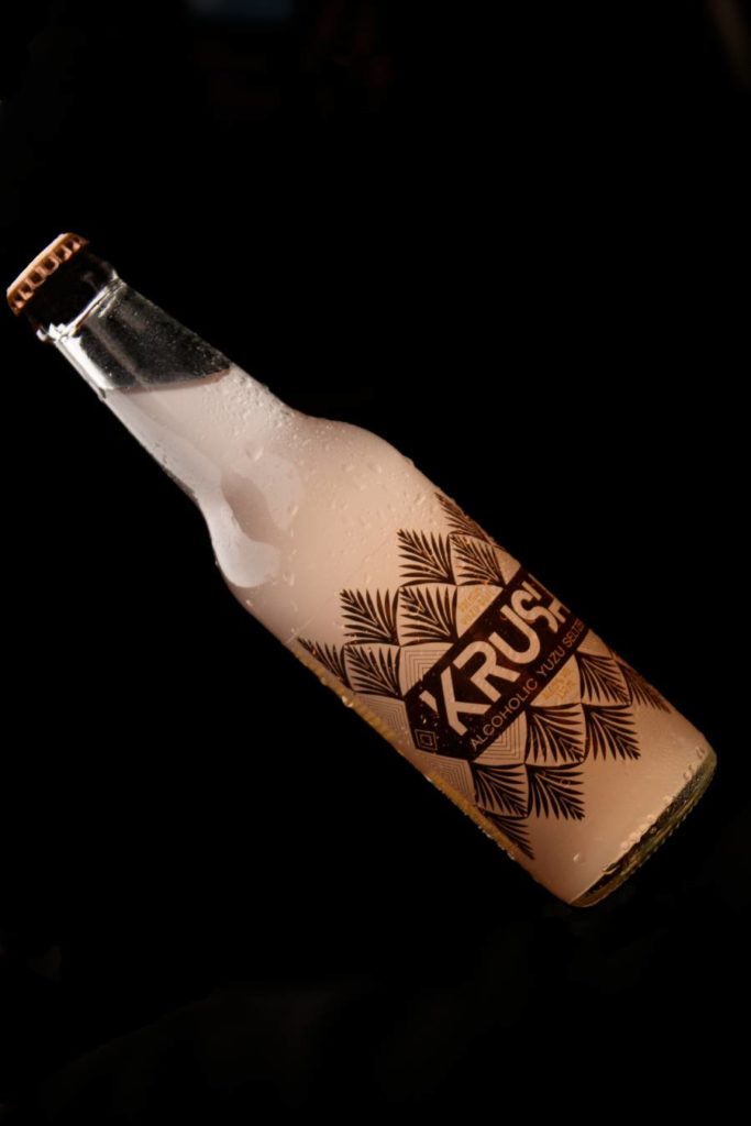 A bottle of KRUSH Premium Fruit Seltzer against black background.